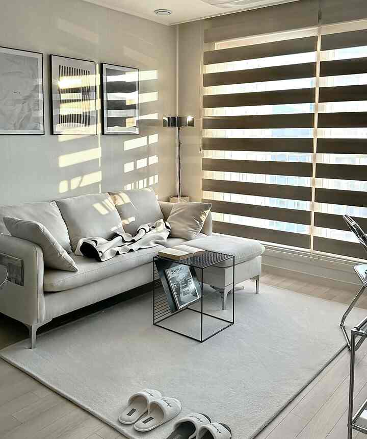 アイボリーとベージュのトーンで構成されたミニマルなリビング、黒いワイヤーフレームのコーヒーテーブルと大きなソファが配置されている印象的な空間