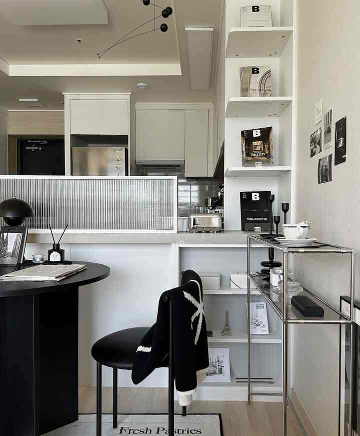 モダンでシンプルな黒と白のトーンのキッチンとリビング空間、黒い丸テーブルと白い棚が配置された清潔感のあるインテリア