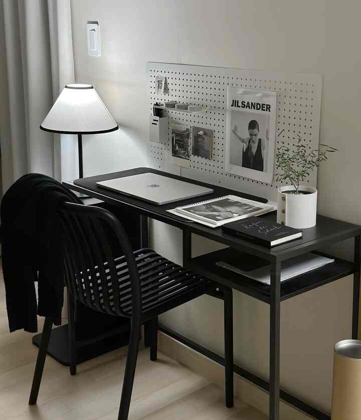 白と黒のトーンが特徴的なホームオフィス、黒いデスクとチェア、壁掛けのパンチングボード、テーブルランプが配置された印象的なワークスペース