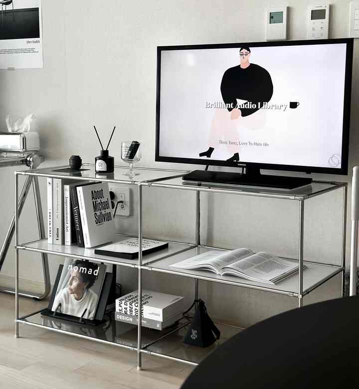 モノトーンのリビング、シルバーのモジュラーシェルフにテレビと黒白の装飾が配置されたシンプルでモダンなインテリア