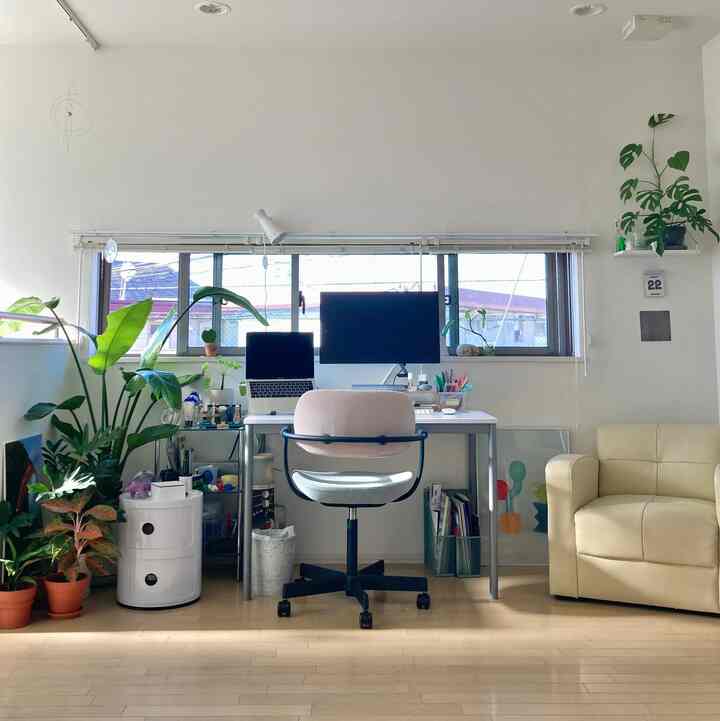 白い壁とナチュラルカラーの床に、ホームオフィス用のデスクとチェア、ソファ、様々な植物が配置されたモダンなリビングスペース