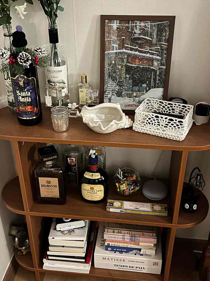 ナチュラルな木目調の寝室の棚に、酒瓶や貝殻のオブジェ、季節のポスターが配置された雰囲気のある空間