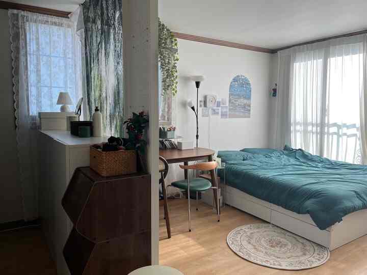 ホワイトとウッドトーンの縦長の寝室、ベッドとデスク、レースカーテンが配置された印象的で実用的な空間