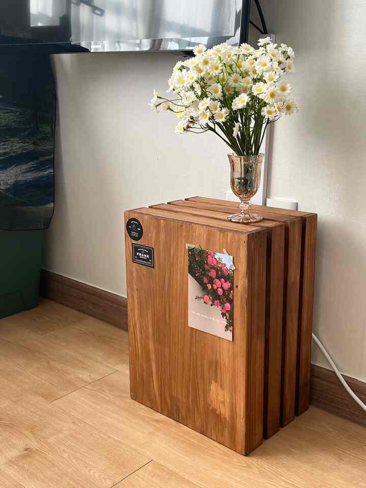 木目調とベージュの空間、木製収納箱の上にカモミールの造花が飾られたシンプルで温かみのあるインテリア