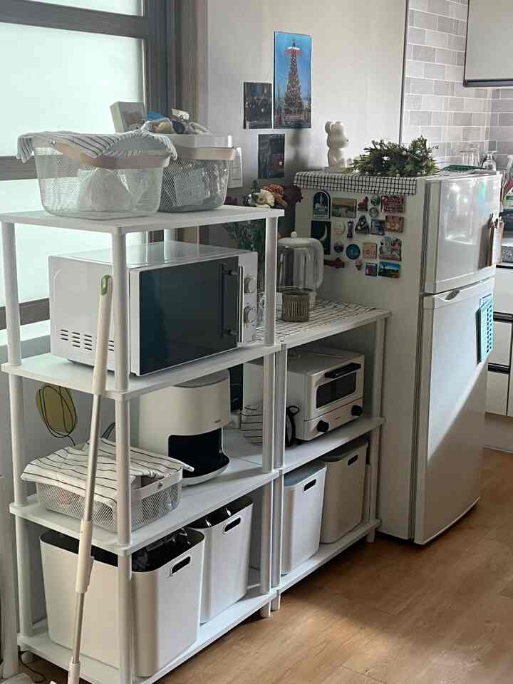 ホワイトとウッドトーンの調和があるキッチン、冷蔵庫横に棚と様々な収納バスケットが整頓された雰囲気のあるインテリア