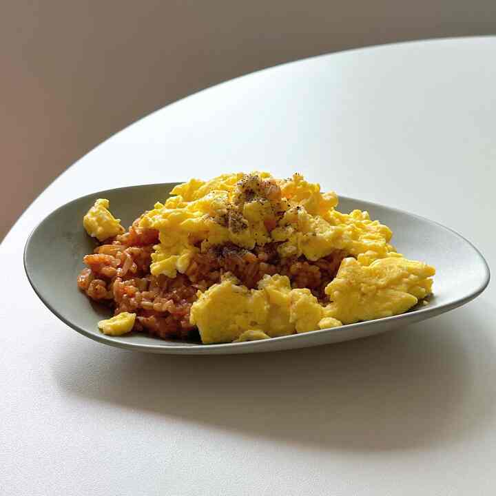 柔らかなベージュ色の天板に黄色のスクランブルエッグとご飯がのった皿が置かれたキッチンテーブル