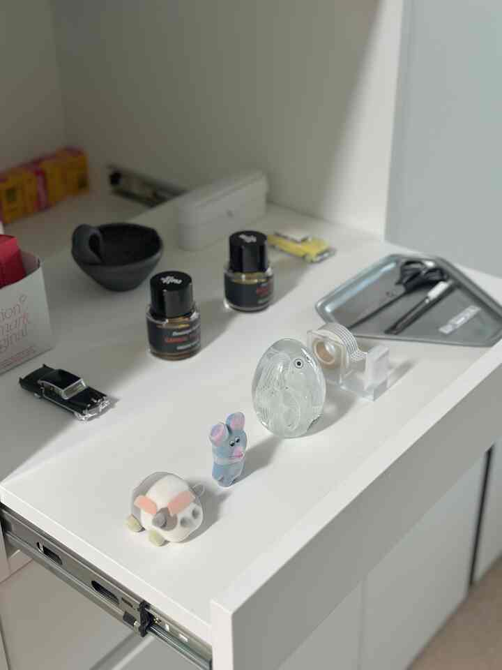 白を基調としたバスルームのキャビネットに香水やテープ、小さなオブジェが配置されたミニマルなインテリア
