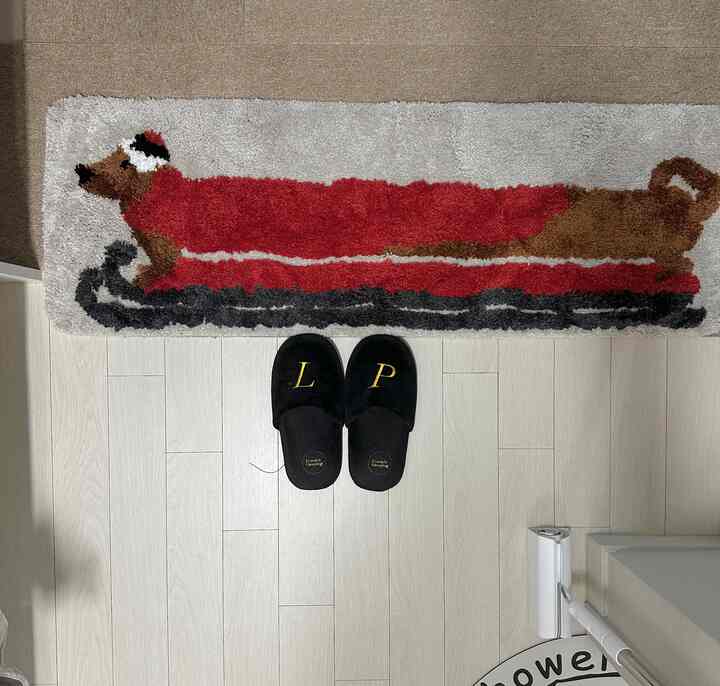 明るい白い床と壁の前に黒い室内履きとクリスマスのサンタ服を着た犬のデザインの長いバスマットが置かれたキッチンスペース