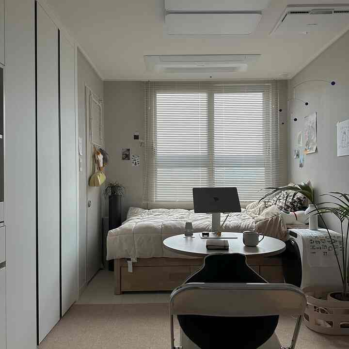 ホワイトとベージュの色調のワンルーム寝室、ベッドと植物が配置された自然なモダンで落ち着いた雰囲気のインテリア