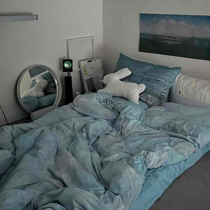 スカイブルーの寝具と白い壁に囲まれた、ベッド上に海の絵が飾られたミニマルな寝室