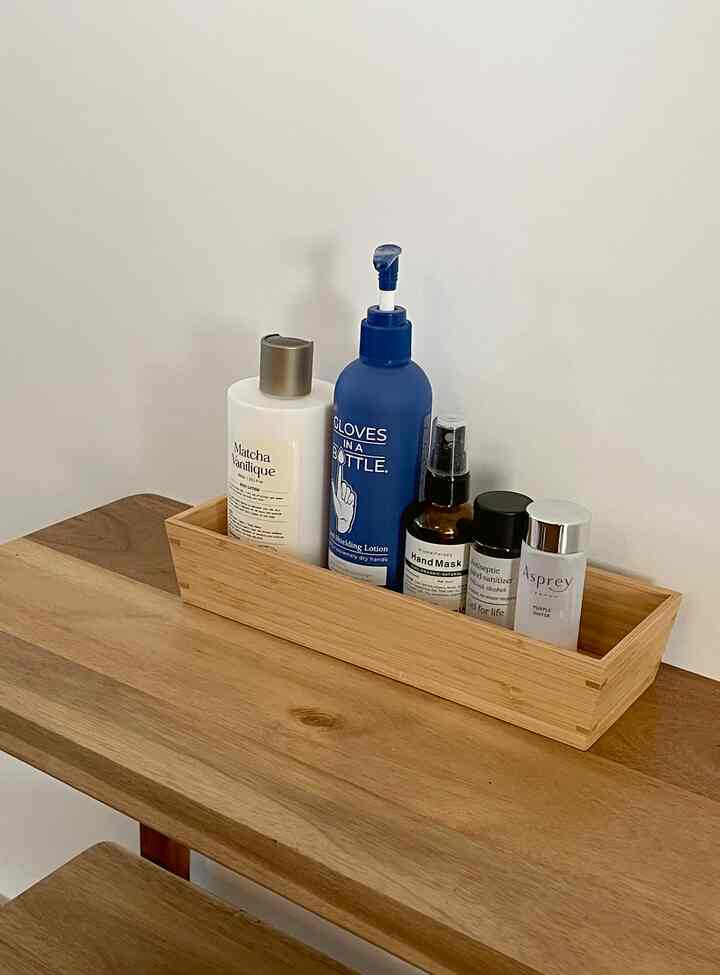 ナチュラルな木目調トレイとテーブルの上に手のクリームと消毒液が整然と配置されたトイレ前の空間