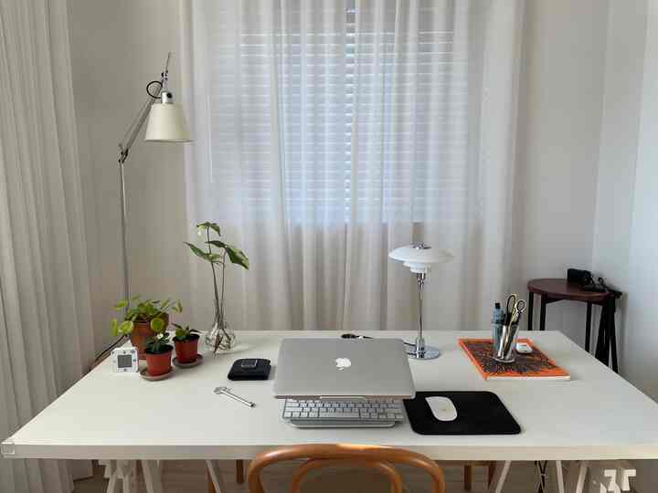 明るい白色調のホームオフィス、中央にノートパソコンとランプが配置されたシンプルなデスク