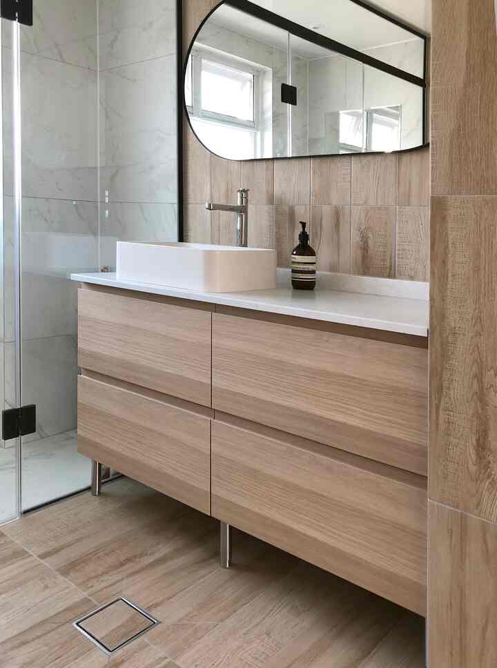 ナチュラルな木目調タイルとホワイトの洗面台が配置されたモダンなバスルーム