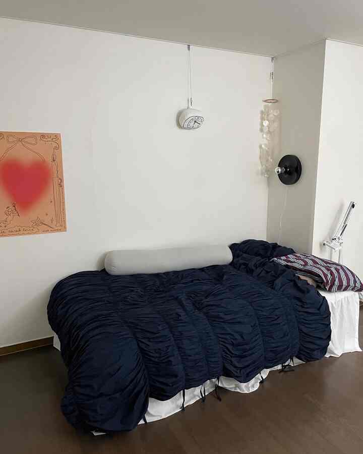 ネイビーの掛け布団カバーが置かれた寝室、中央に大きなベッドと壁掛け照明と時計が配置されたミニマルなインテリア