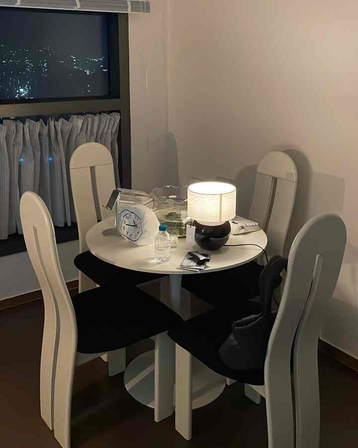 白い丸テーブルと椅子が配置されたダイニングルーム、中央に暖かく灯るテーブルランプが印象的な空間