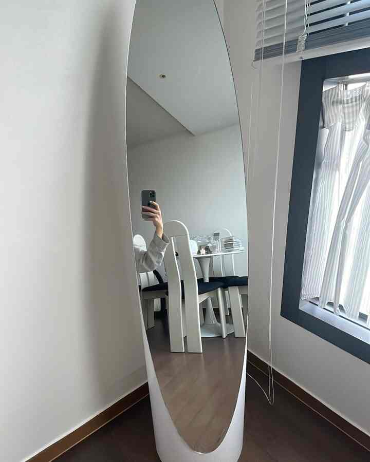 白と木目調が調和したダイニングルームの、縦長の空間に設置された縦長の全身鏡とブラインドがあるシンプルなインテリア