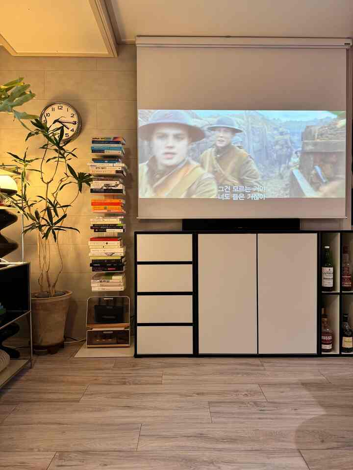 ナチュラルカラーのリビング、大きなプロジェクタースクリーンとキャビネットが配置された居心地の良いホームシネマ空間