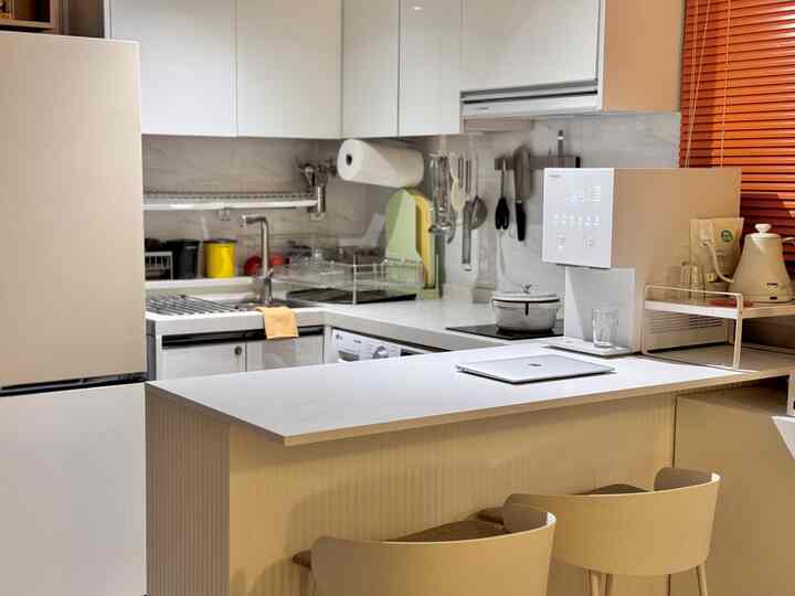 明るいホワイトトーンのモダンなワンルームキッチン、中央にダイニングカウンターと椅子が配置された印象的な空間