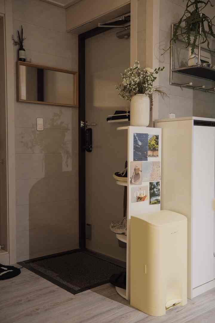 ナチュラルカラーの狭い玄関、コーナーシェルフと靴収納、明るいゴミ箱と植物が配置された雰囲気のある空間