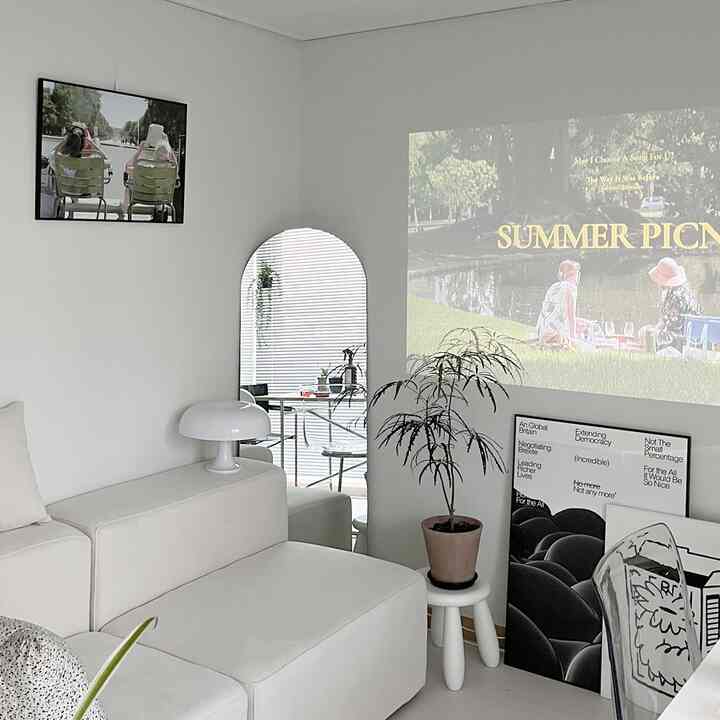 白を基調としたリビング、シンプルなソファと額縁、植物が配置されたミニマルでナチュラルな雰囲気のあるインテリア