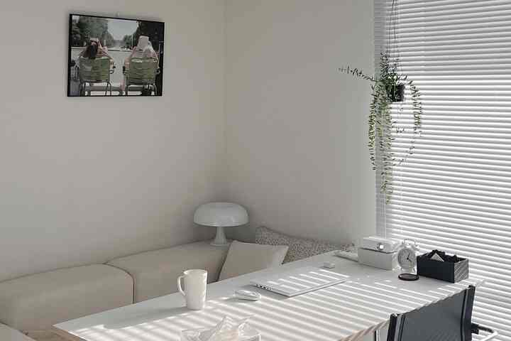 白とベージュのトーンが特徴のリビング兼ホームオフィス空間、ソファとダイニングテーブル、ブラインド、植物が配置されたモダンなインテリア