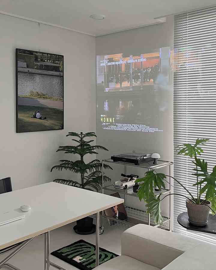 白と緑のトーンのリビング、モダンな雰囲気のソファ、テーブル、ブラインド、植物が配置された印象的な空間