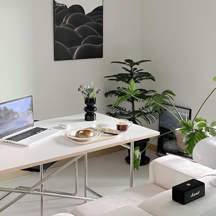 白とナチュラルトーンのリビング兼おうちカフェ空間、ミニマルなダイニングテーブルとソファ、植物が配置された落ち着いた雰囲気のインテリア