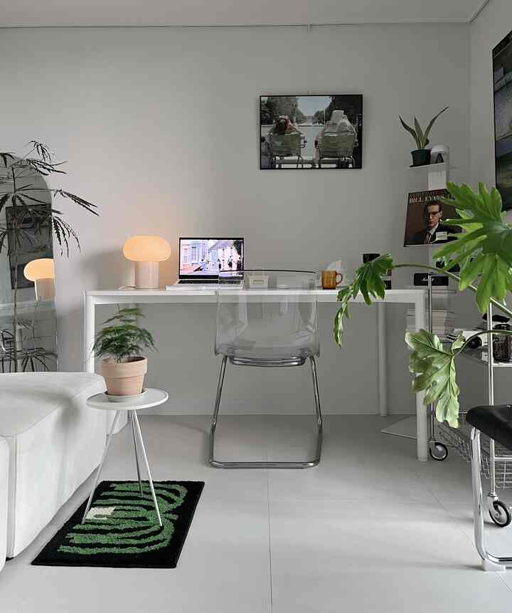 白を基調としたリビング兼ホームオフィス、透明な椅子と植物が配置されたミニマルなインテリア