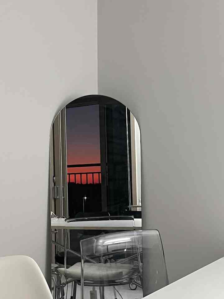 ホワイトの壁に設置された長方形の鏡と透明なプラスチックチェアが配置されたシンプルなミッドセンチュリーモダンのダイニング空間