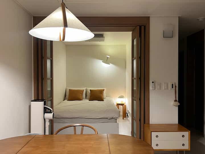 ホワイトと木目調が調和した寝室、ベッドとスツールナイトテーブルが配置されたミニマルなインテリア