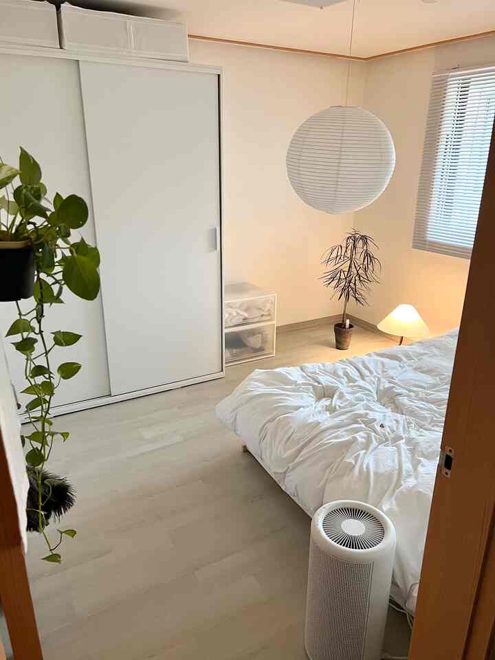 ホワイトとナチュラルカラーの寝室、スライディングワードローブとベッド、フロアランプ、植物が配置された清潔感と抜け感のあるインテリア