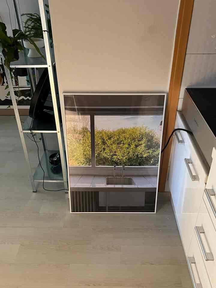 ホワイトとナチュラルウッド調のキッチンスペース、壁に立てかけられたA1サイズの額縁が印象的なシンプルモダンなインテリア