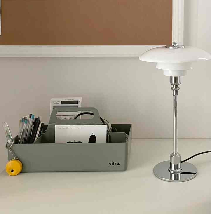 白とシルバーのトーンのホームオフィスデスク、ツールボックスとテーブルランプが整然と配置された印象的な空間