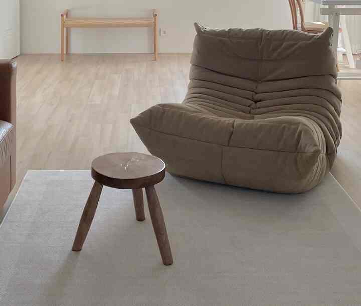 ナチュラルなウッドトーンのリビングルーム、ブラウンのラウンジチェアとコーヒーテーブルとして使われる小さな木製スツールが配置された落ち着いた空間