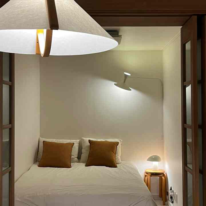 白と茶色のトーンの寝室、壁掛け照明と木製スツールが配置されたモダンで温かみのある雰囲気のインテリア