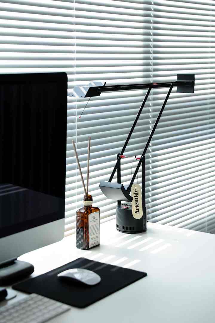 白と黒のトーンのホームオフィス、コンピューターとディフューザー、テーブルランプが配置されたシンプルで明るい作業空間