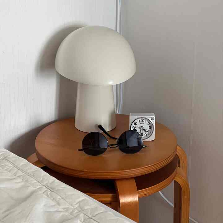 ホワイトとブラウンのトーンが特徴の寝室のナイトテーブルに、テーブルランプと時計が置かれた落ち着いた空間