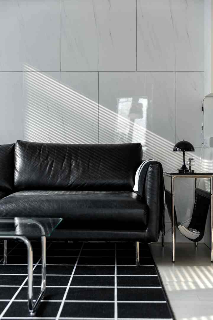 ブラックとホワイトの色調が特徴のリビング、レザーソファとグリッド柄のラグ、ステンレス脚のソファとサイドテーブルが配置されたモダンなインテリア