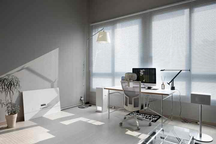 モノトーンの白とグレーを基調としたコンパクトなホームオフィス、シンプルなデスクと椅子、フロアランプが配置された落ち着いた書斎のインテリア