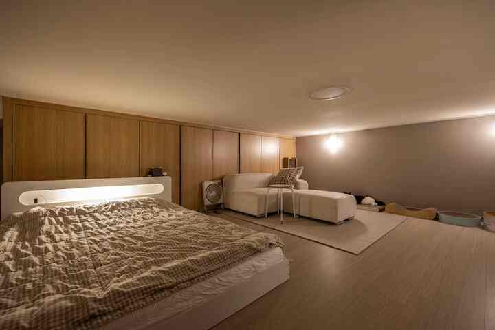 ベージュ色調のロフト寝室、ソファとスツールが配置され、猫の爪とぎなどのペット用品がある居心地の良い空間