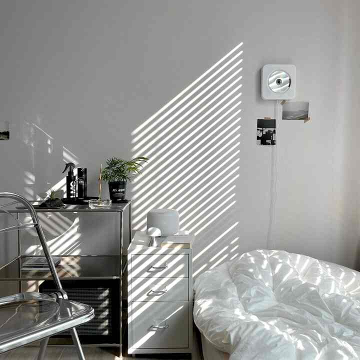 白を基調とした寝室、透明な折りたたみ椅子と金属製の収納棚が配置されたミニマルで清潔感あるインテリア