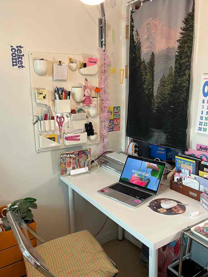 白い壁とデスクが配置された小さな玄関スペース、大きな森林風景のファブリックポスターと透明な椅子が印象的な実用的なインテリア