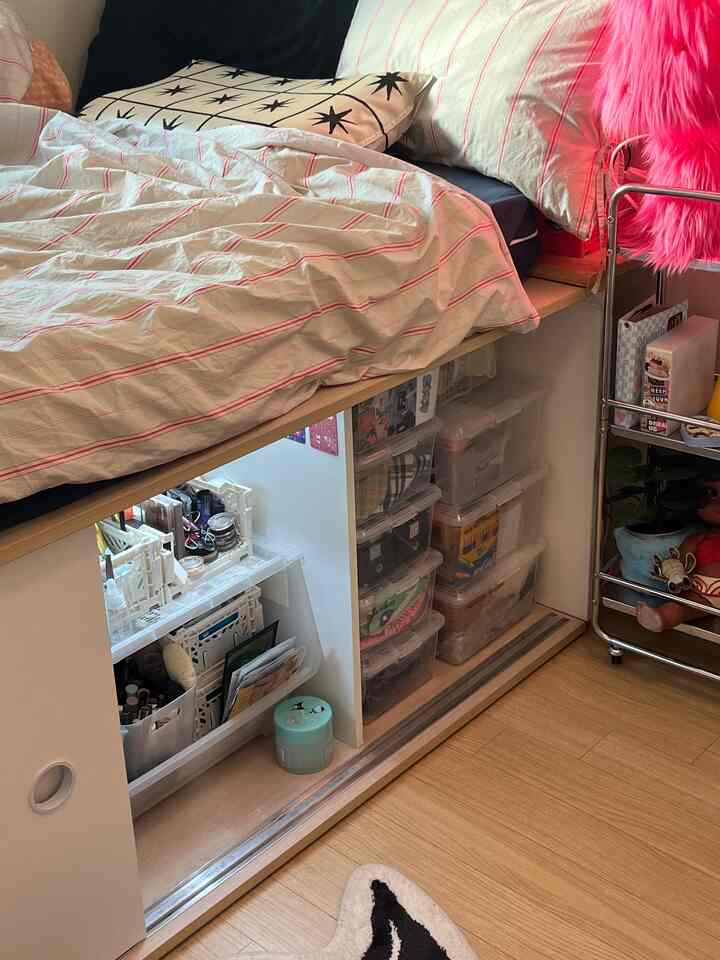 ウッドトーンとピンクのアクセントがある寝室、折り畳み収納ボックスと透明な収納箱が配置された整理された空間