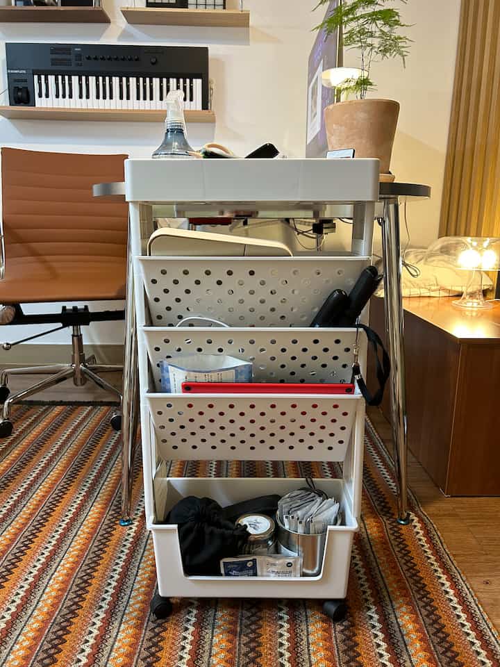 ナチュラルな木目調フローリングと白いトロリーが配置されたホームオフィスの書斎空間、ブラウンのオフィスチェアと作業用キーボードが実用的な雰囲気を演出