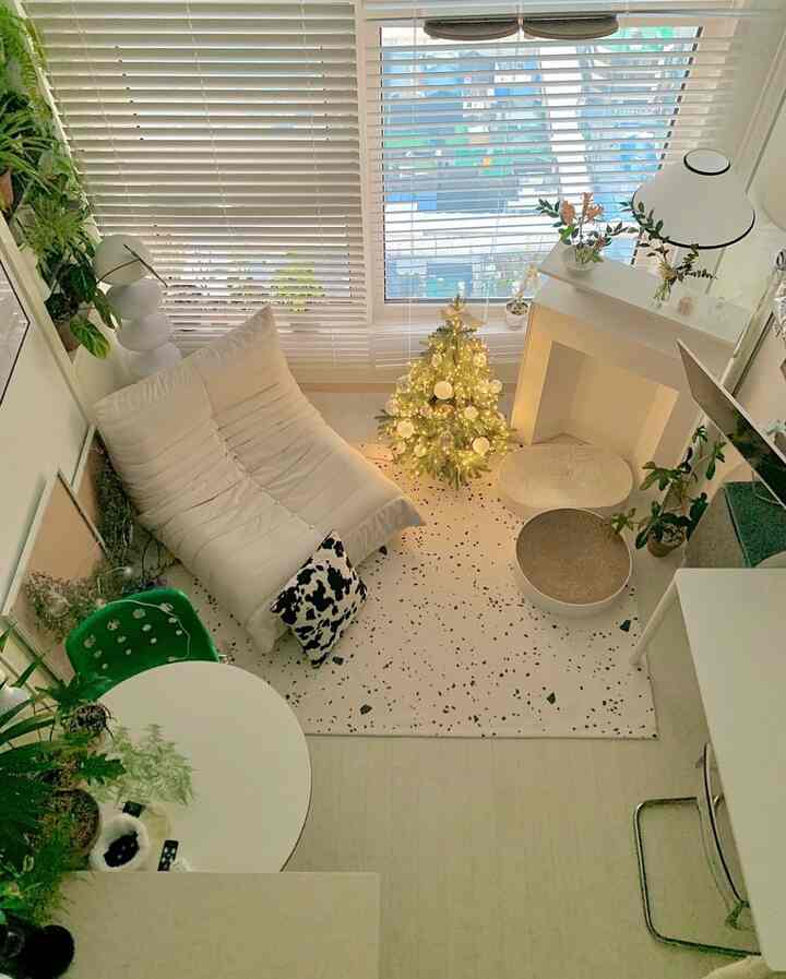 明るいホワイトとウッドトーンのナチュラルなリビング、植物と小さなクリスマスツリー、シンプルなソファとラグが配置された温かみのある雰囲気のあるインテリア