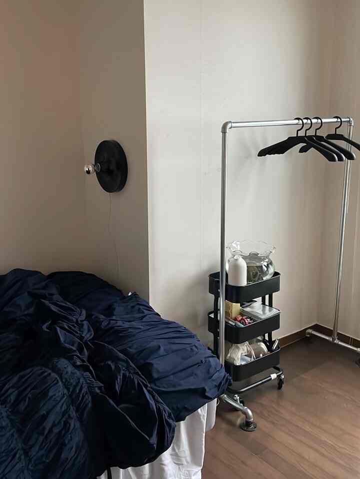 ネイビーの掛け布団カバーがある寝室、シンプルな金属製コートラックと壁のブラケットライトが配置されたミニマルな空間
