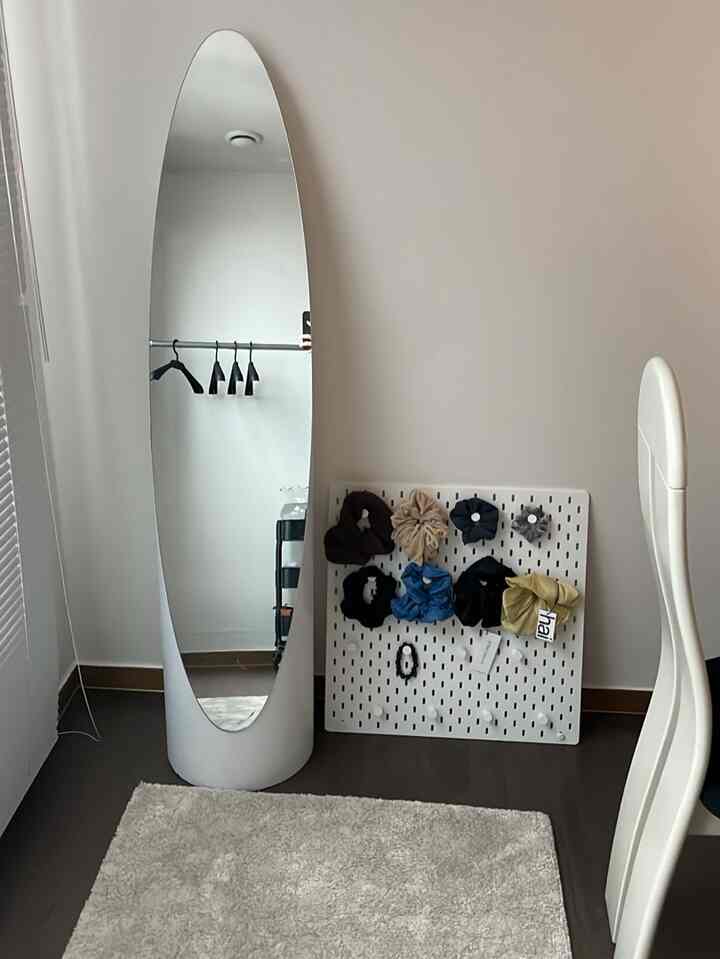 白い壁とミニマルな家具があるコンパクトな部屋、全身鏡とペグボードに小物が配置された整った空間