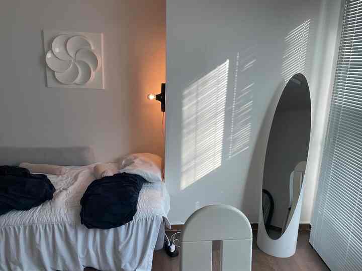 ホワイトとネイビーの色調の寝室、ベッドとブラインド、壁照明が白い壁に温かみのある雰囲気を演出するインテリア