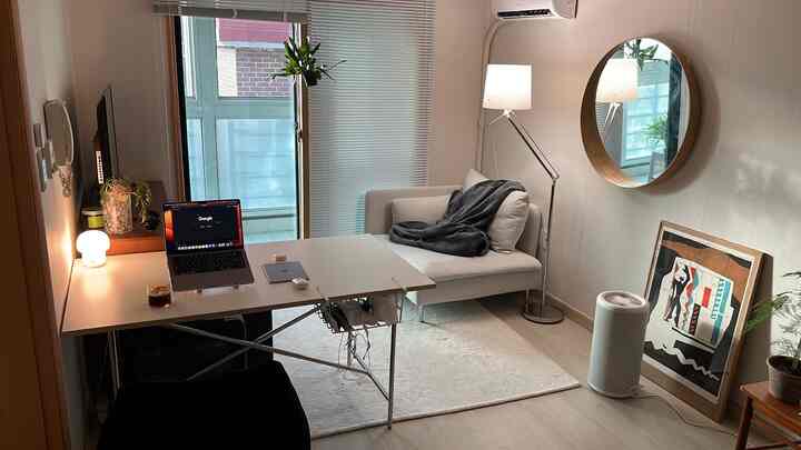 白とナチュラルカラーの一人暮らしリビング、机とソファが配置されたシンプルでホームオフィスの雰囲気のある空間