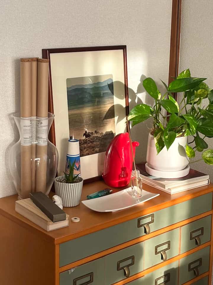 温かみのあるナチュラルカラーのチェストに緑の観葉植物と赤いオブジェが置かれた雰囲気のあるインテリアコーナー